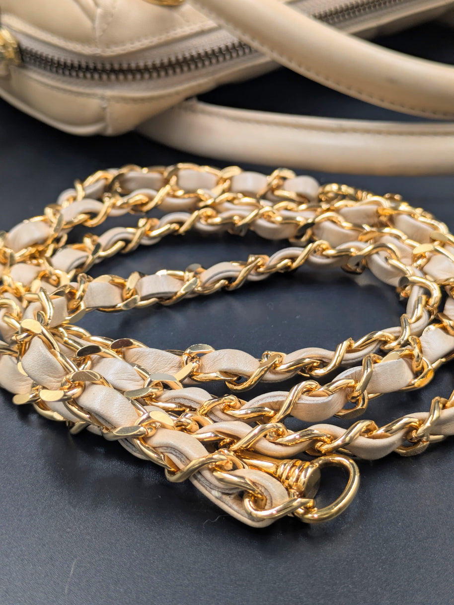 Gros plan sur la chaîne dorée entrelacée de cuir et l’anse du sac Chanel beige