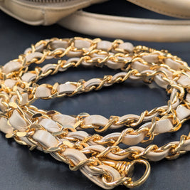 Gros plan sur la chaîne dorée entrelacée de cuir et l’anse du sac Chanel beige