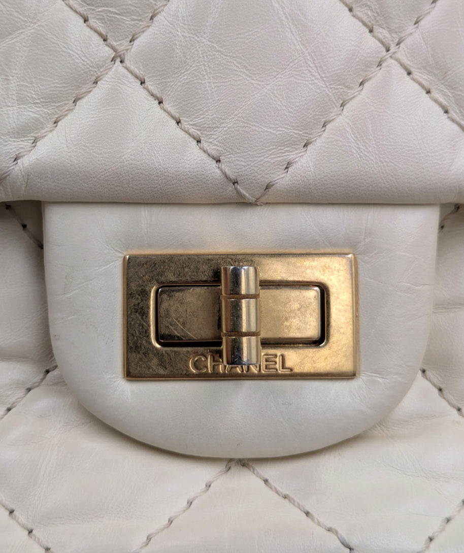 Gros plan sur le fermoir Mademoiselle doré gravé CHANEL du sac 2.55 écru