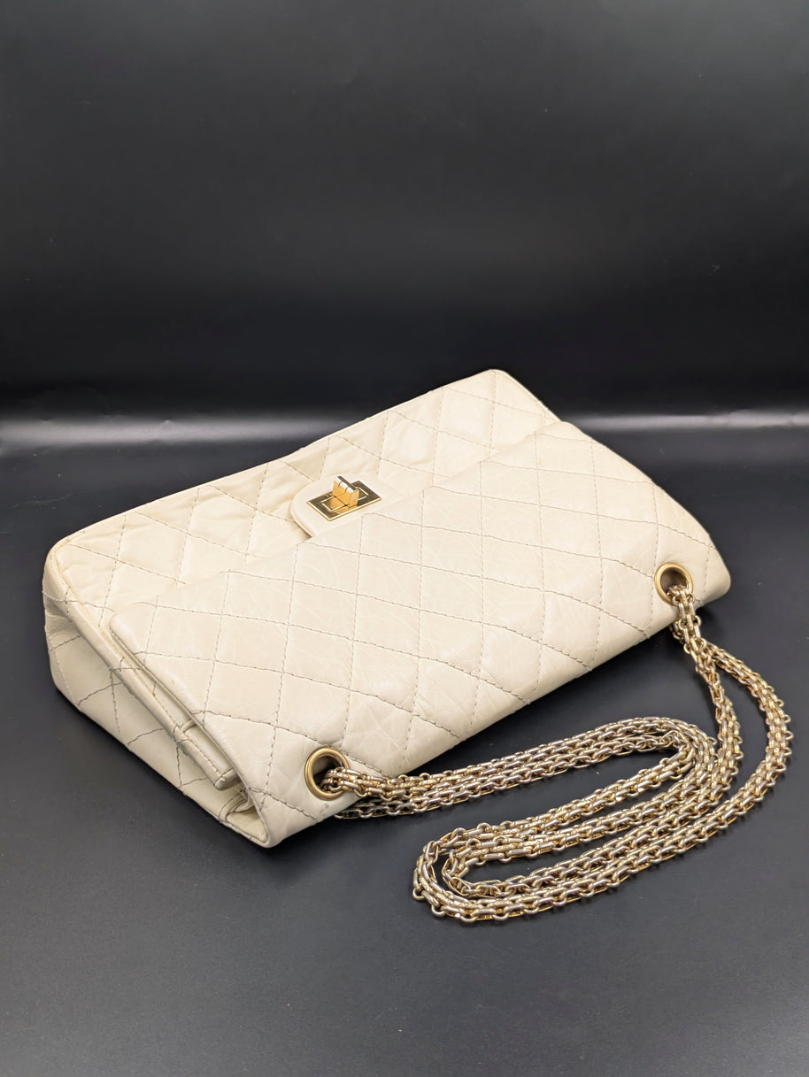Sac Chanel 2.55 écru posé en biais avec sa double chaîne dorée