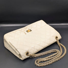 Sac Chanel 2.55 écru posé en biais avec sa double chaîne dorée